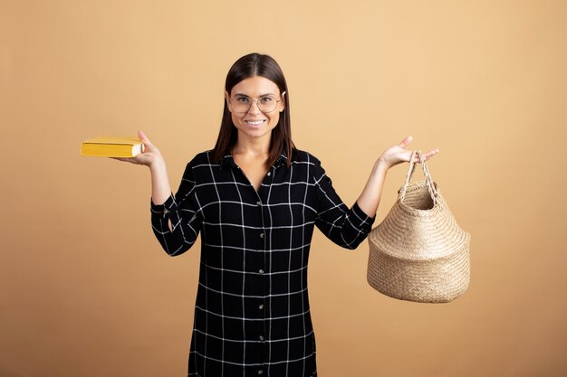 Une Jeune Femme Vêtue D'une Robe à Carreaux Se Dresse Avec Un Sac En Osier Sur Fond Orange