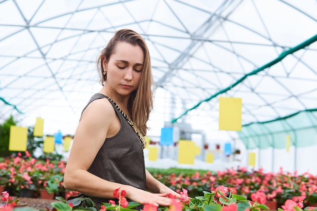 Une jeune femme vêtue d'une robe touche avec amour des fleurs dans une serre