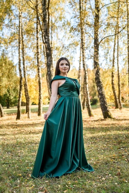 Jeune femme vêtue d'une robe verte à la mode marchant dans le parc de l'automne.