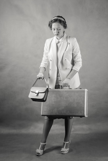 Photo jeune femme vêtue de style rétro avec valise et sac à main studio tourné en noir et blanc