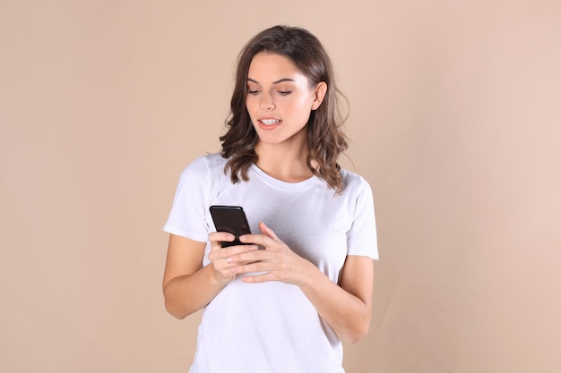 Jeune femme vêtue de vêtements de base isolée sur fond beige, utilisant un téléphone portable