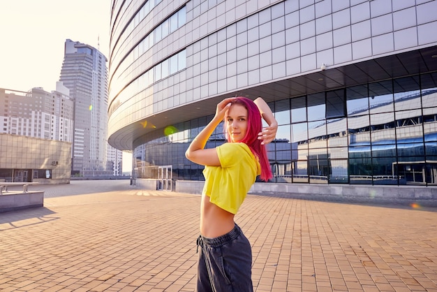 Une jeune femme vêtue de vêtements de sport brillants et de cheveux roses teints danse en ville
