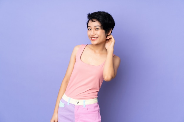 Jeune femme vietnamienne aux cheveux courts sur mur violet rire