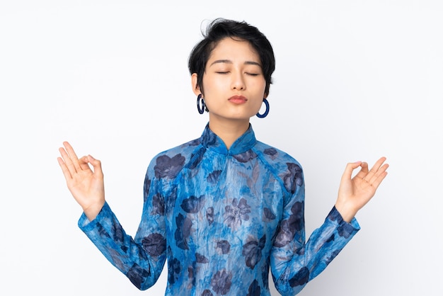 Jeune femme vietnamienne aux cheveux courts portant une robe traditionnelle sur blanc isolé dans une pose zen