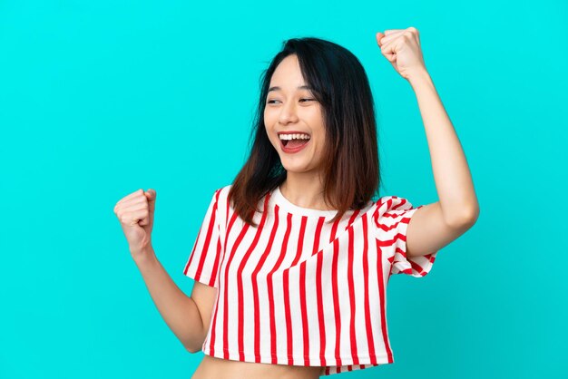 Jeune femme vietnamienne isolée sur fond bleu célébrant une victoire