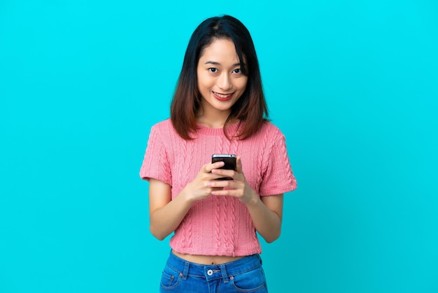 Jeune femme vietnamienne isolée sur fond bleu envoyant un message avec le mobile