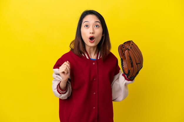 Jeune femme vietnamienne de joueur avec le gant de base-ball d'isolement sur le fond jaune recherchant et avec l'expression étonnée