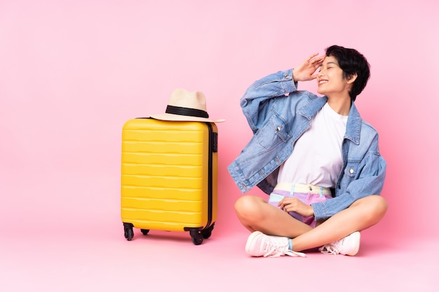 Jeune femme vietnamienne avec valise assise sur le sol sur le mur rose a réalisé quelque chose et a l'intention de la solution