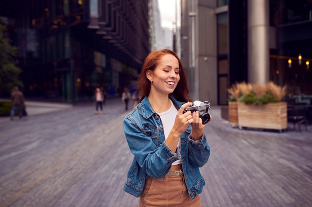 Jeune femme en ville prenant une photo sur un appareil photo numérique pour publier sur les médias sociaux