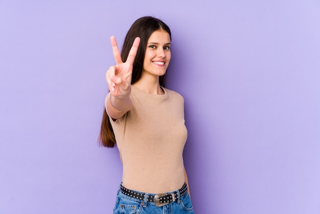 Jeune femme sur violet joyeux et insouciant montrant un symbole de paix avec les doigts.