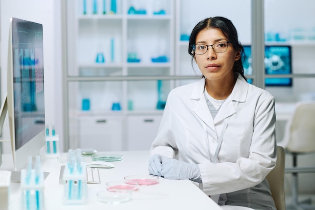 Jeune femme virologue ou microbiologiste sérieuse en blanchon regardant la caméra