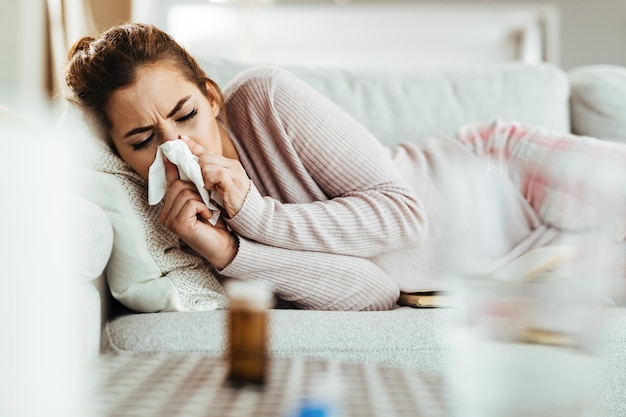 Jeune femme avec le virus de la grippe allongée sur un canapé et se moucher