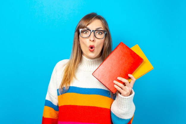 Jeune femme avec un visage surpris détient des livres dans ses mains sur un fond bleu