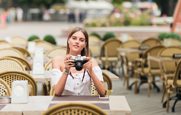 Jeune femme vive tient l'ancien appareil photo rétro dans ses mains alors qu'il était assis à la table dans un café en plein air