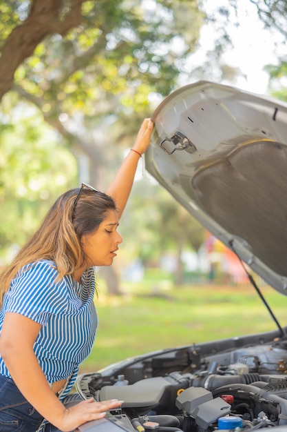 Photo une jeune femme voit pourquoi sa voiture s'est cassée avec le capot ouvert.