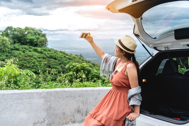 Jeune femme voyageur assise à l'arrière de la voiture et prenant une photo de selfie