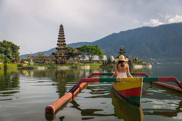 Jeune femme voyageur pagayant sur un bateau en bois à Pura Ulun Danu Bratan