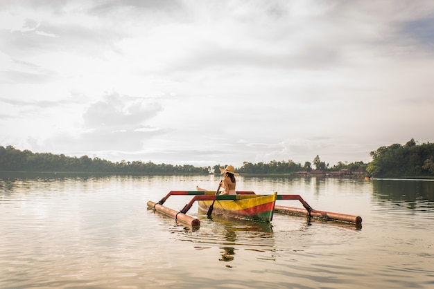 Jeune femme voyageur pagayant sur un bateau en bois à Pura Ulun Danu Bratan