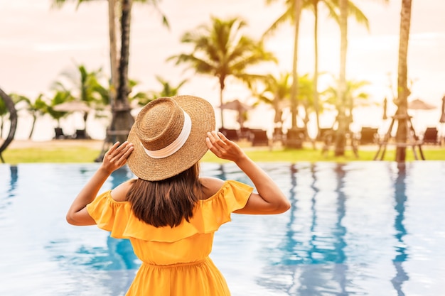 Jeune femme voyageur se détendre et profiter du coucher du soleil au bord d'une piscine tropicale lors d'un voyage pour les vacances d'été