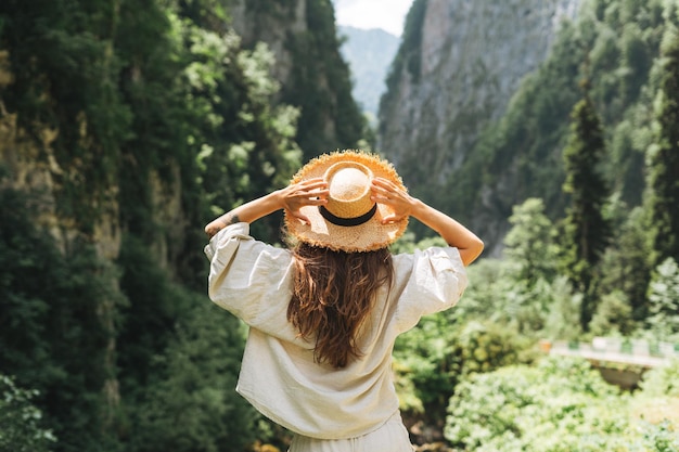 Une jeune femme voyageuse aux longs cheveux blonds en chapeau de paille regarde une belle vue sur les montagnes