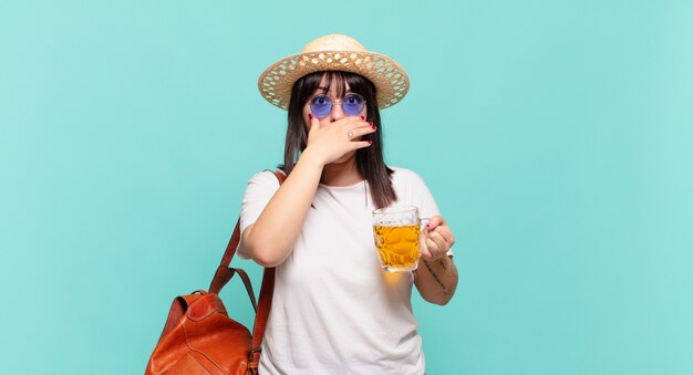 Jeune femme voyageuse couvrant la bouche avec les mains avec une expression choquée et surprise, gardant un secret ou disant oups