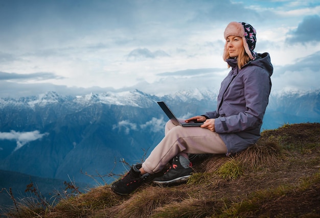 Une jeune femme voyageuse indépendante travaille partout en ligne à l'aide d'un ordinateur portable et profite de la vue