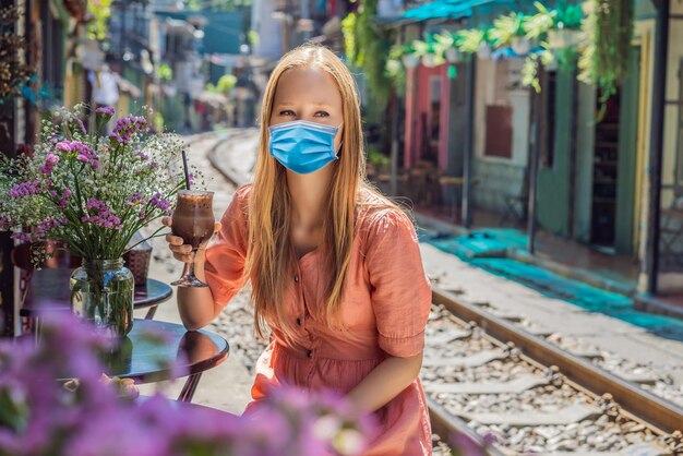 Jeune femme voyageuse portant un masque médical pendant le coronavirus covid boit du café assis près de la