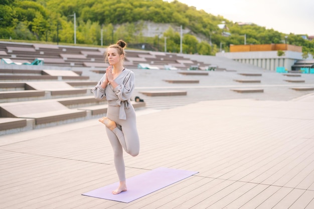 Jeune femme yogini assez flexible pratiquant le yoga debout sur une jambe qui s'étend à l'extérieur par temps nuageux