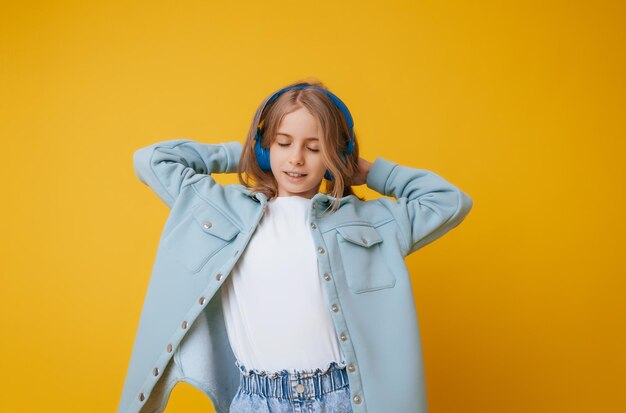 Une jeune fille de 1113 ans au casque écoute de la musique et danse en studio sur fond jaune