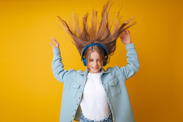 Une jeune fille de 1113 ans au casque écoute de la musique et danse en studio sur fond jaune