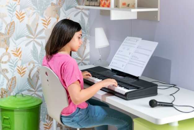 Jeune fille absorbée jouant de la musique sur un clavier électronique à la suite d'une partition au-dessus de l'instrument dans un concept de passe-temps récréatif ou d'apprentissage de la musique