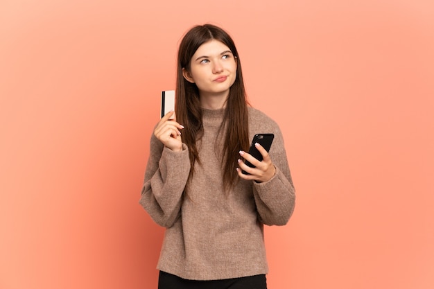 Jeune fille achetant avec le mobile avec une carte de crédit tout en pensant