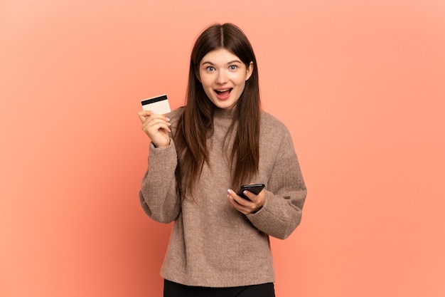 Jeune fille achetant avec le mobile et tenant une carte de crédit avec expression surprise