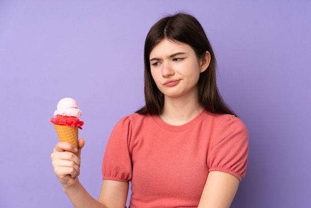 Jeune fille adolescente ukrainienne tenant une glace au cornet sur un mur violet isolé avec une expression triste