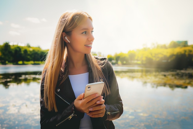 Jeune fille adulte de succès caucasien souriant heureux marchant dans le parc avec tablette et téléphone