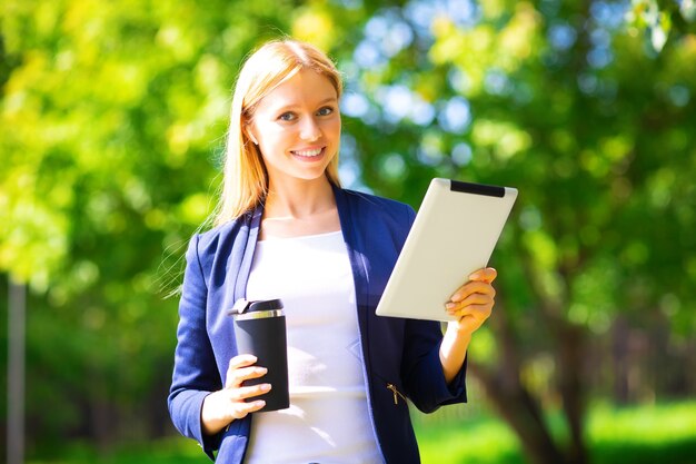 Jeune fille adulte de succès caucasien souriant heureux marchant dans le parc avec tablette et téléphone