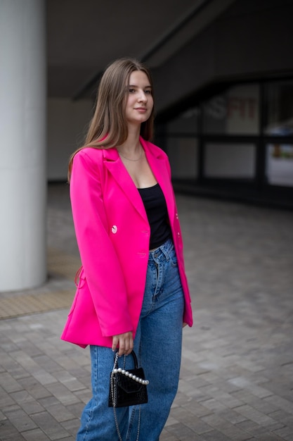 une jeune fille d'affaires vêtue d'une veste fuchsia brillante et d'un jean se tient à pleine hauteur dans la rue