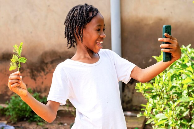 une jeune fille africaine excitée tenant un téléphone portable et une plante