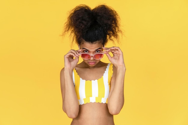 Jeune fille africaine de mode femme noire afro cheveux porter élégant lunettes de soleil roses lunettes regardant la caméra publicité lunettes de vente isolées en été fond de studio jaune portrait espace de copie