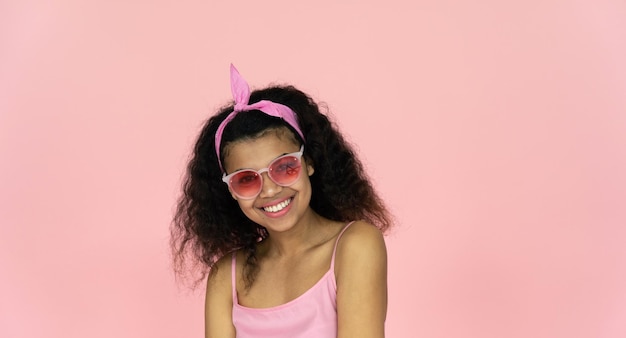 Une jeune fille africaine à la mode porte des lunettes isolée sur un mur rose.