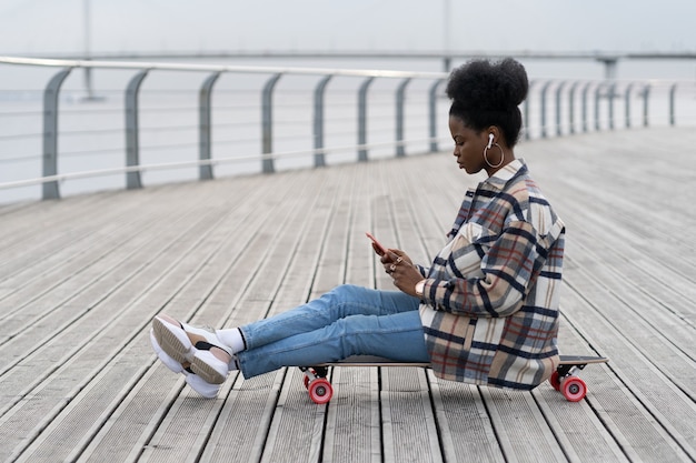 Jeune Fille Africaine S'asseoir Sur Un Longboard Avec Un Smartphone Dans Le Texte à La Main En Plein Air Dans Le Parc à L'aide D'une Connexion G