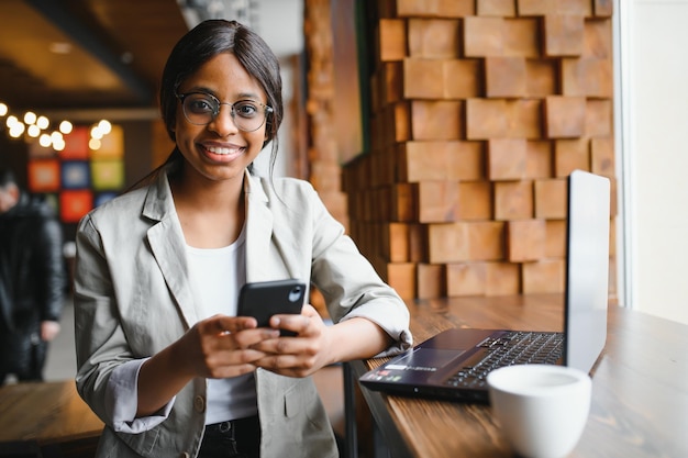 Jeune fille afro-américaine assise au restaurant et tapant sur son ordinateur portable Jolie fille travaillant sur ordinateur au café