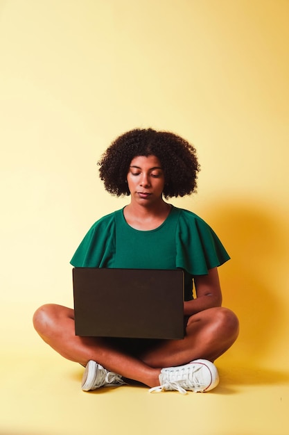 Photo jeune fille afro-américaine avec des cheveux afro assise à regarder une technologie de concept d'ordinateur portable