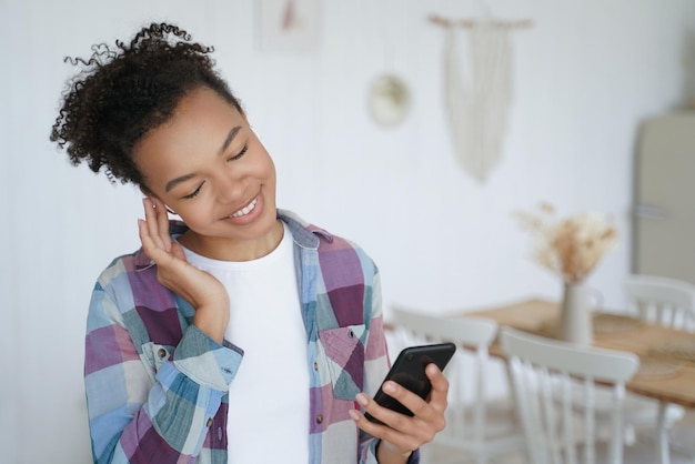 Une jeune fille afro-américaine écoute de la musique à l'aide d'un smartphone à la maison Publicité pour des applications musicales