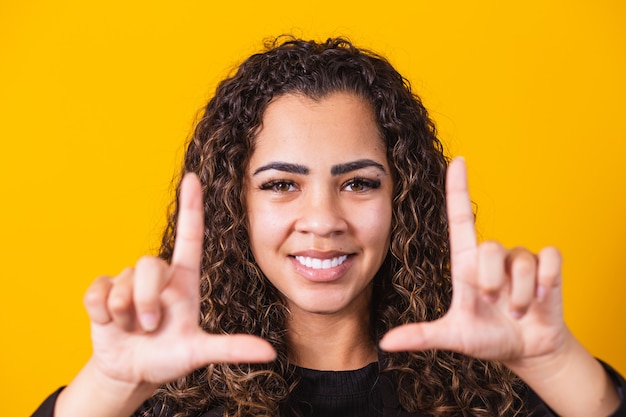 Jeune fille afro-américaine portant des vêtements de direction souriante faisant un cadre photo avec les mains et les doigts avec un visage heureux. concept de créativité et de photographie.