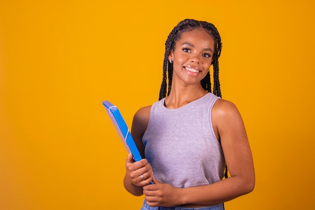 Jeune fille afro souriante heureuse étudiante adolescente tenant des livres et des cahiers sur fond avec espace libre pour le texte