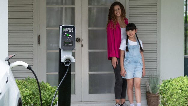 Une jeune fille aide sa mère à recharger sa voiture électrique à la maison Synchronos