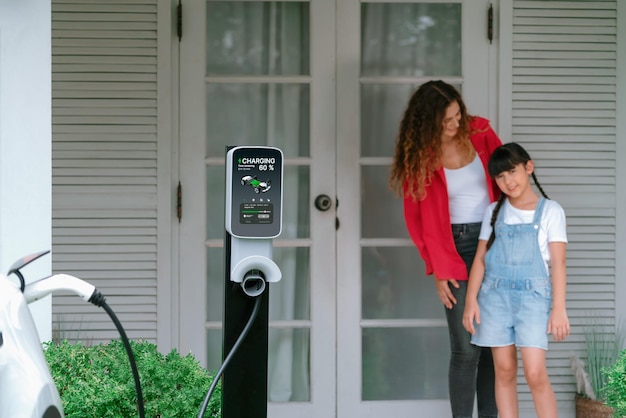 Une jeune fille aide sa mère à recharger sa voiture électrique à la maison Synchronos