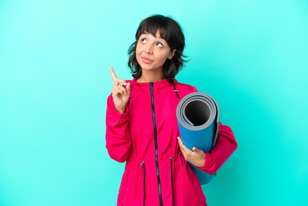 Jeune fille allant à des cours de yoga tout en tenant un tapis isolé sur fond bleu pointant vers le haut une excellente idée