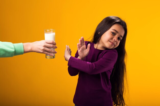 Photo une jeune fille allergique aux produits laitiers montre un geste d'arrêt devant un verre de lait sur fond jaune concept d'intolérance au lactose